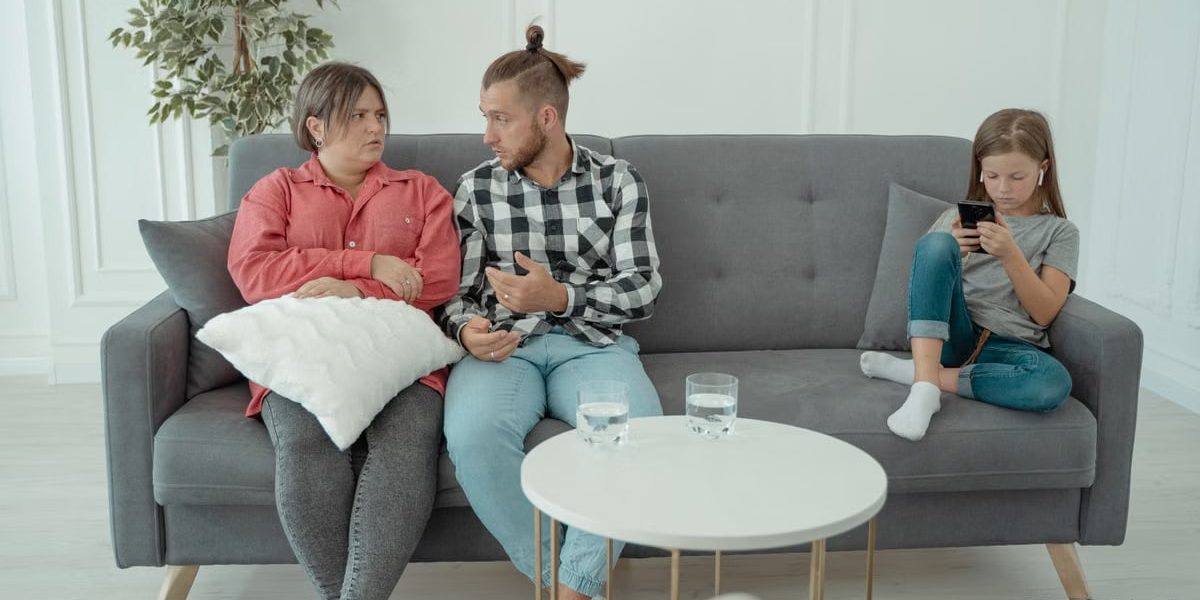 A family therapy session with parents discussing things while a child is absorbed in her smartphone.