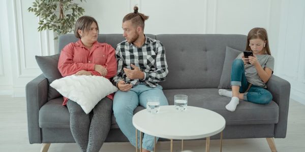 A family therapy session with parents discussing things while a child is absorbed in her smartphone.