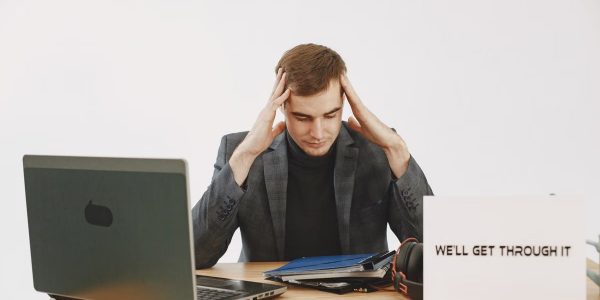 Young man in home office feeling stressed, working during pandemic with motivational message by his side.